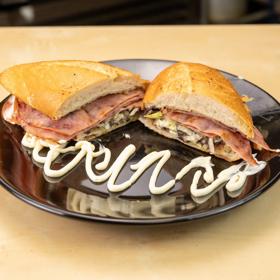 Toasted ham sandwich with lettuce and creamy sauce, cut in half on a black plate with mayonnaise drizzle.