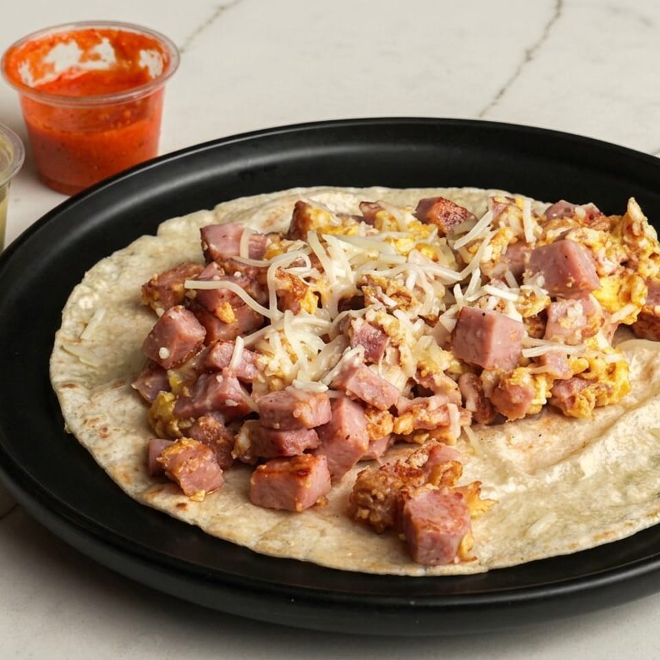 Flour tortilla topped with diced sausage, scrambled eggs, and shredded cheese on a black plate, served with green and red salsa.